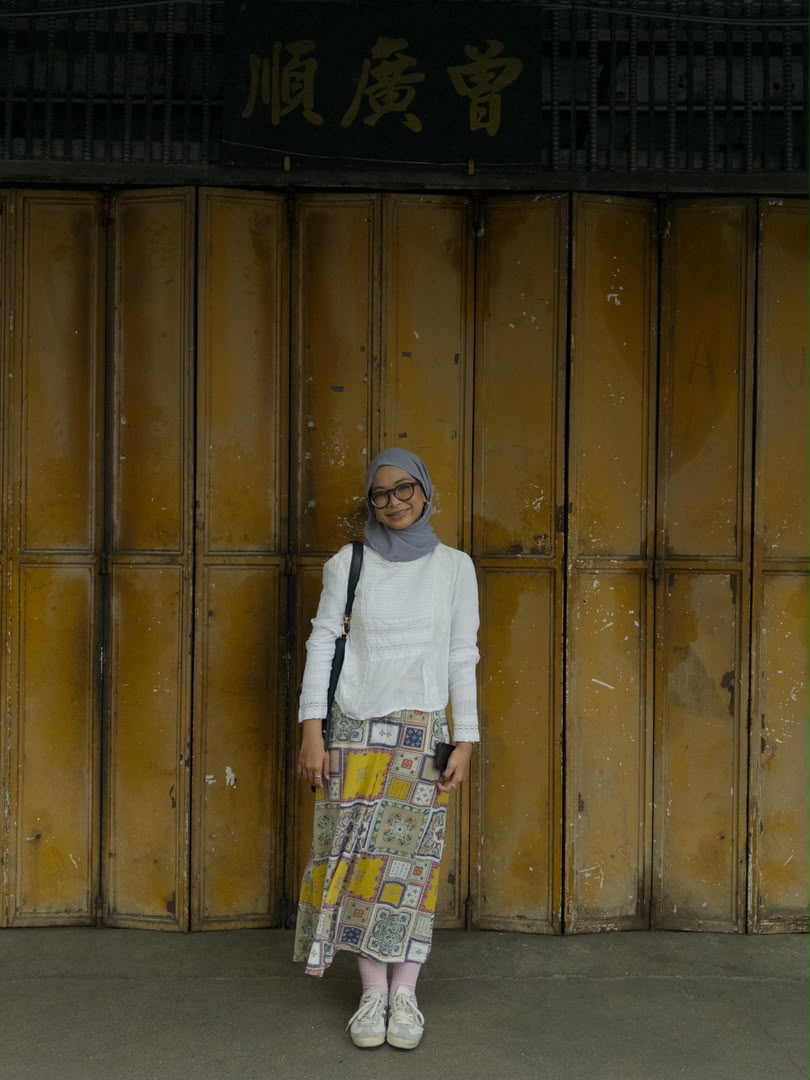 Husna berdiri depan kedai lama berwarna kuning